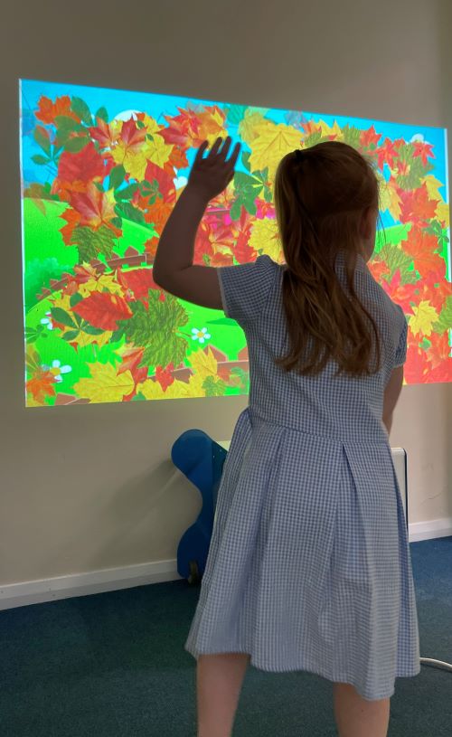 School girl using gesture interaction by engaging with the scatter activity on the wall