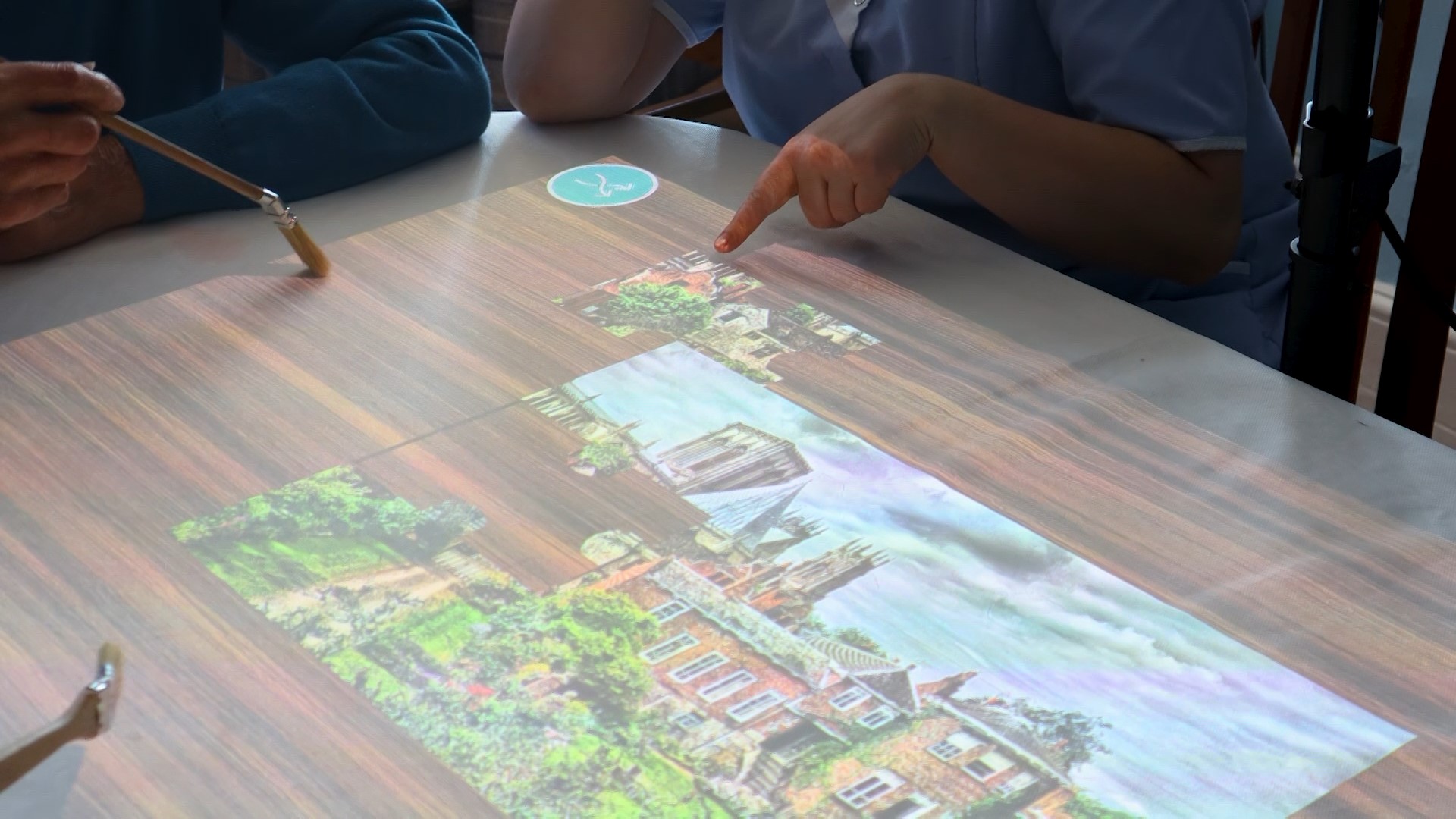 An interactive table with jigsaw activity, as the user touches the jigsaw pieces they fall into place, seated around the table is an elderly gentlemen with car provider.
