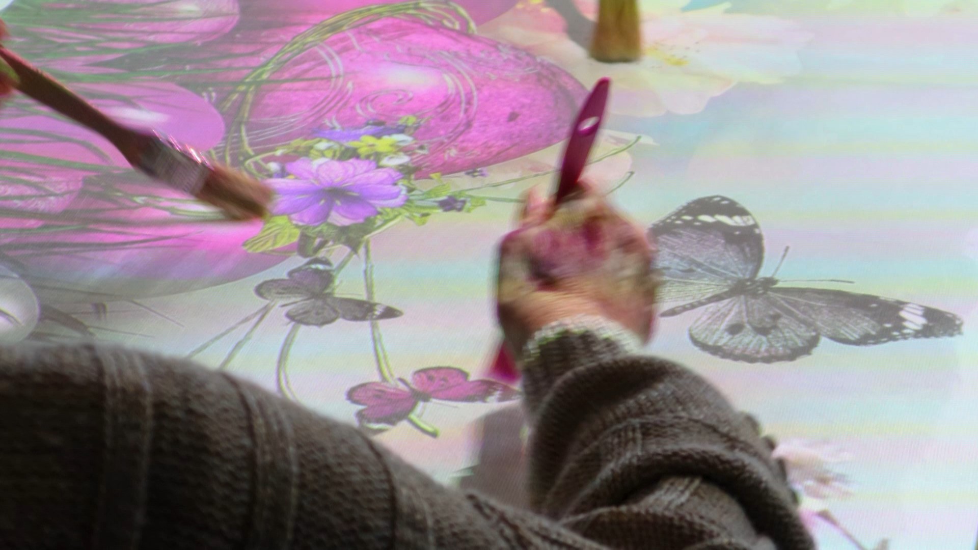 A care home resident using a paintbrush to carefully colour in the vibrant butterflies being projected on to the table in front of them from an interactive table projector.