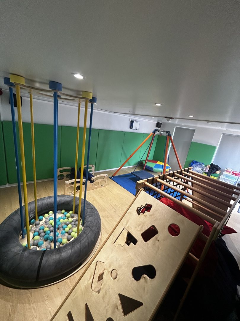 A sensory integration room, the room features a jump and play island for promoting physical development, a climbing frame which provides a safe environment for children to climb and balance. The room also has green soft padded walls for safety and a occupational therapy swing located in the corner